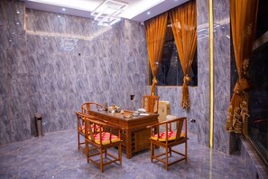 A room with a marble wall, a wooden dining table with chairs, and a window with curtains.