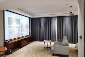 A modern living room with a large flat-screen TV, a grey sofa, a small round table, and a dark curtain backdrop. - Jingan Haoting Hotel (Gengma)