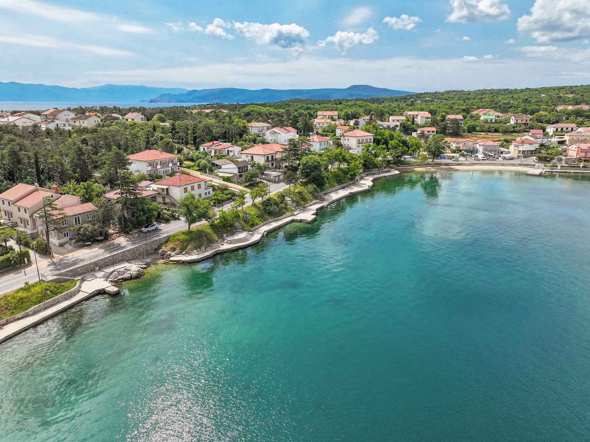 A coastal town with houses along a waterfront, a clear sky, and mountains in the background.