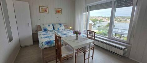 A bedroom with a bed, a table, chairs, a window with a view, and a radiator.