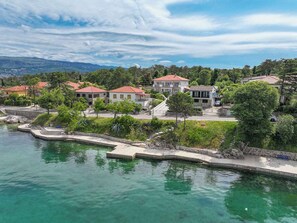 A coastal residential area with houses along a waterfront, featuring a clear view of the sea and a stone pathway leading to the water.