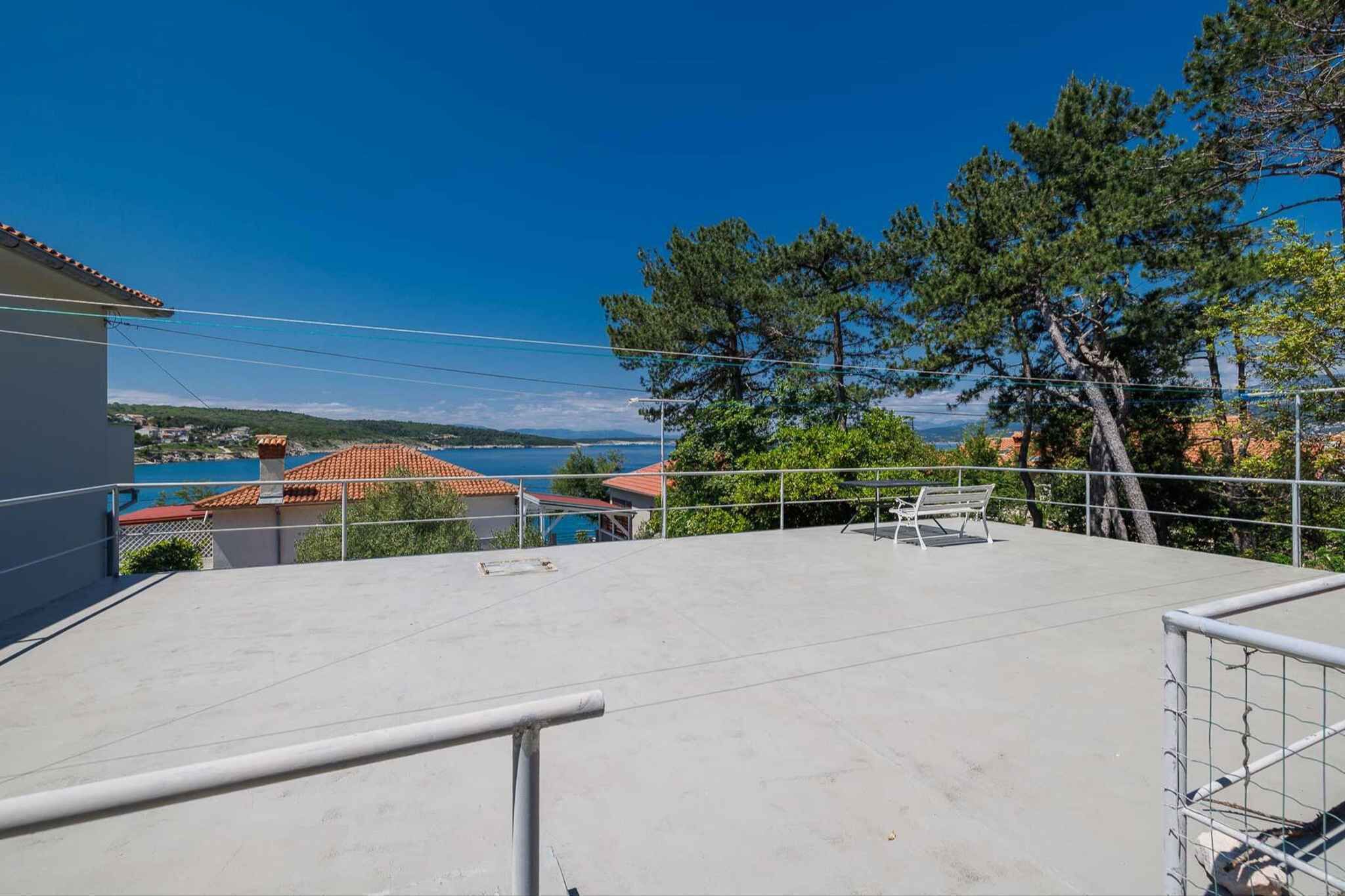 A rooftop terrace with a clear view of a coastal town, a metal railing, and a bench.
