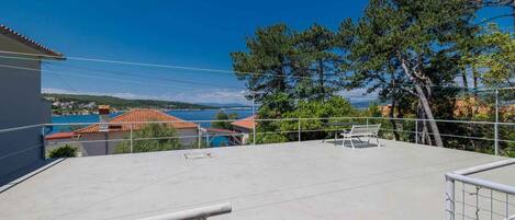 A rooftop terrace with a clear view of a coastal town, a metal railing, and a bench.