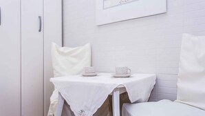 A small, white, two-seater table with a white tablecloth and two cups on it, positioned next to a white cabinet and a white chair. - Holiday apartment with sea view (Šilo)