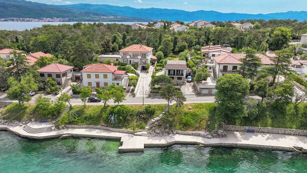 A coastal residential area with houses, clear turquoise water, and a mountainous backdrop. - Holiday apartment with sea view (Šilo)