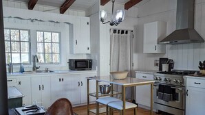 A kitchen with white cabinets, a wooden table, a stove, and a hanging light fixture. - Dreamy Cottage right on the Lake, Dog Friendly! (Lake Waccamaw)