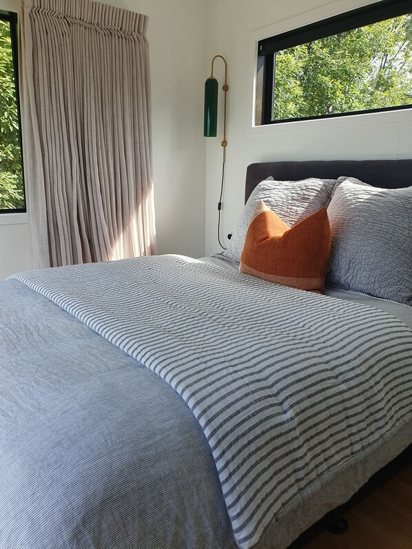 A neatly made bed with striped bedding, a dark headboard, and a window with a view of trees.