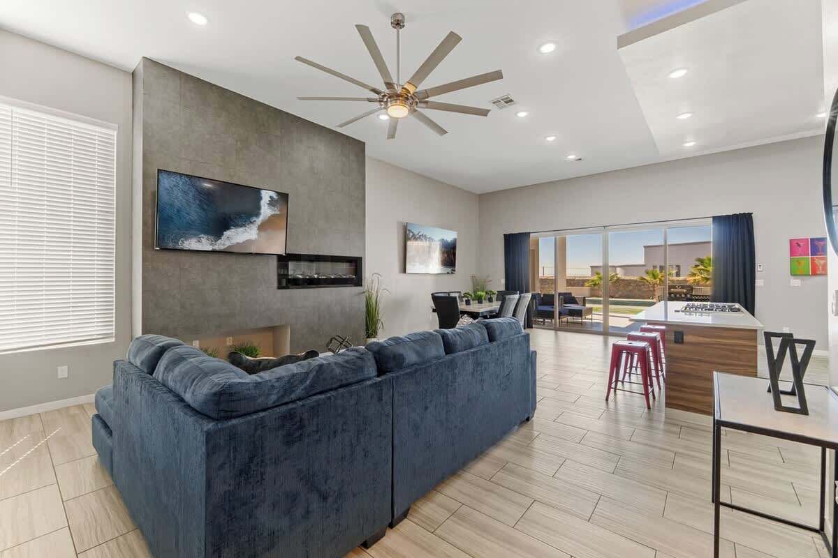 A modern living room with a large dark blue sofa, a ceiling fan, and a flat-screen TV mounted on the wall.