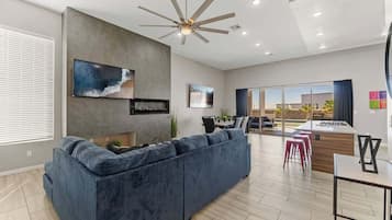 A modern living room with a large dark blue sofa, a ceiling fan, and a flat-screen TV mounted on the wall.