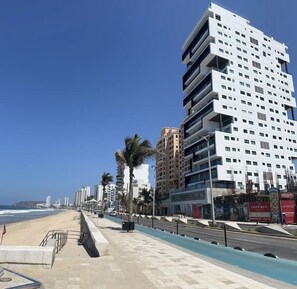 A coastal cityscape with modern high-rise buildings, a beach, and a promenade.