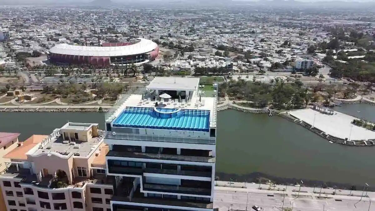 A high-rise hotel with a rooftop pool and a view of a stadium and cityscape.