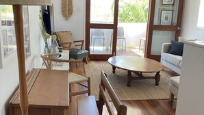 Una sala acogedora con un banco de madera, una mesa y un sofá. Hay un ventilador de techo, una ventana con vistas a la vegetación y una puerta que da al exterior.