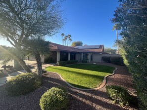 A house with a solar panel roof, surrounded by well-maintained landscaping and palm trees. - Big Game House Rental in Glendale! 5bed/3bath - Pool, Putting Green & Much More! (Glendale)