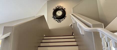 Una escalera con escalones blancos y barandillas de madera que conduce a un rellano con un reloj fijado a la pared.