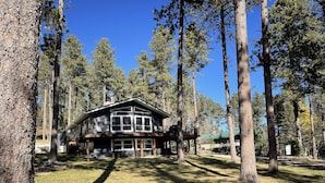 A two-story cabin with a deck, surrounded by tall pine trees. - Trailer & Parking Friendly, 24x56  Garage, 5-bedroom, 3-bath, Newly renovated! (Lead)