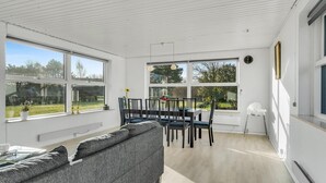 A bright, sunlit room with a dining table and chairs, a sofa, and large windows offering a view of the outdoors. - Nice home in Rudkøbing with kitchen (Rudkøbing)