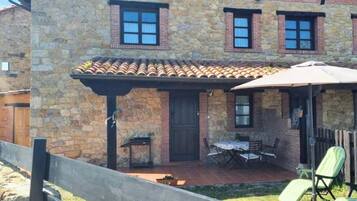 Un edificio de piedra con un patio que tiene mobiliario exterior y una pérgola.