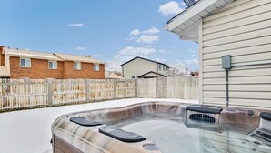 Un jacuzzi en un patio trasero con una valla de madera, una casa y un cielo despejado.
