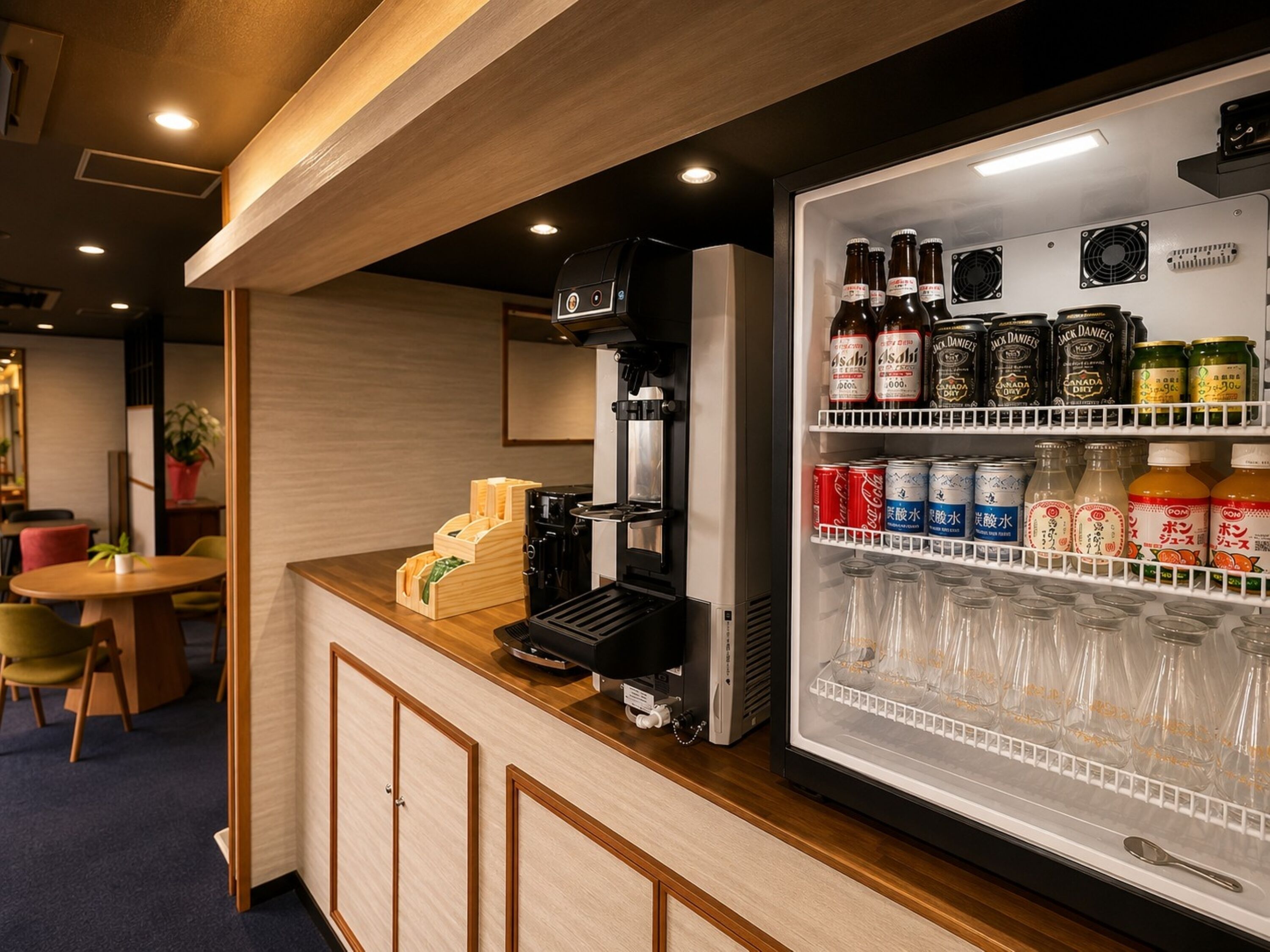 A bar area with a coffee machine, a refrigerator stocked with beverages, and a seating area with chairs and a table.