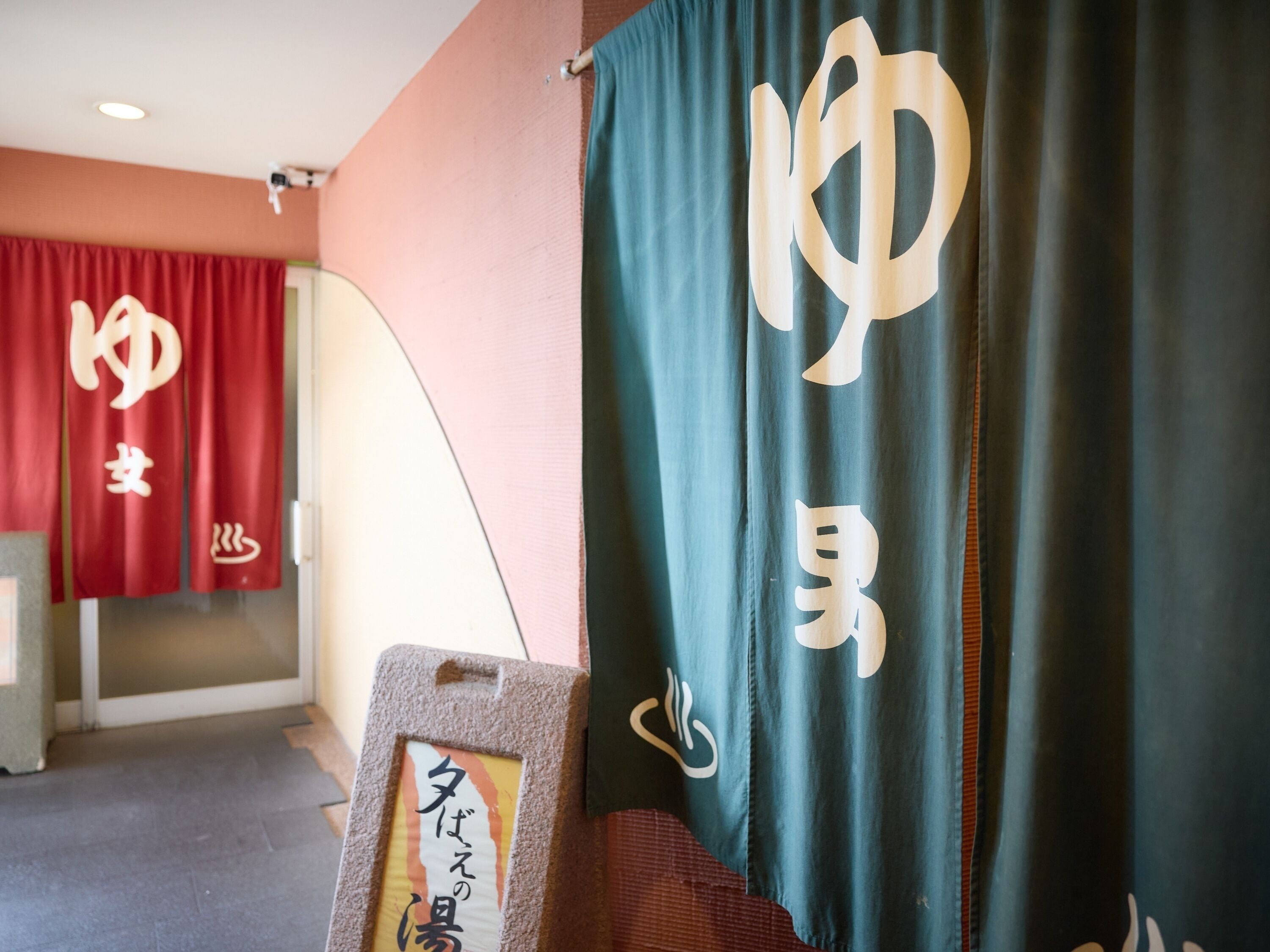 Une pièce avec un rideau rouge et un rideau vert foncé orné de lettres blanches. On y trouve un panneau avec du texte en japonais, posé sur un support.