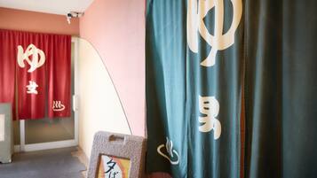 A room with a red curtain and a dark green curtain with white text. There is a sign with Japanese text on a stand.