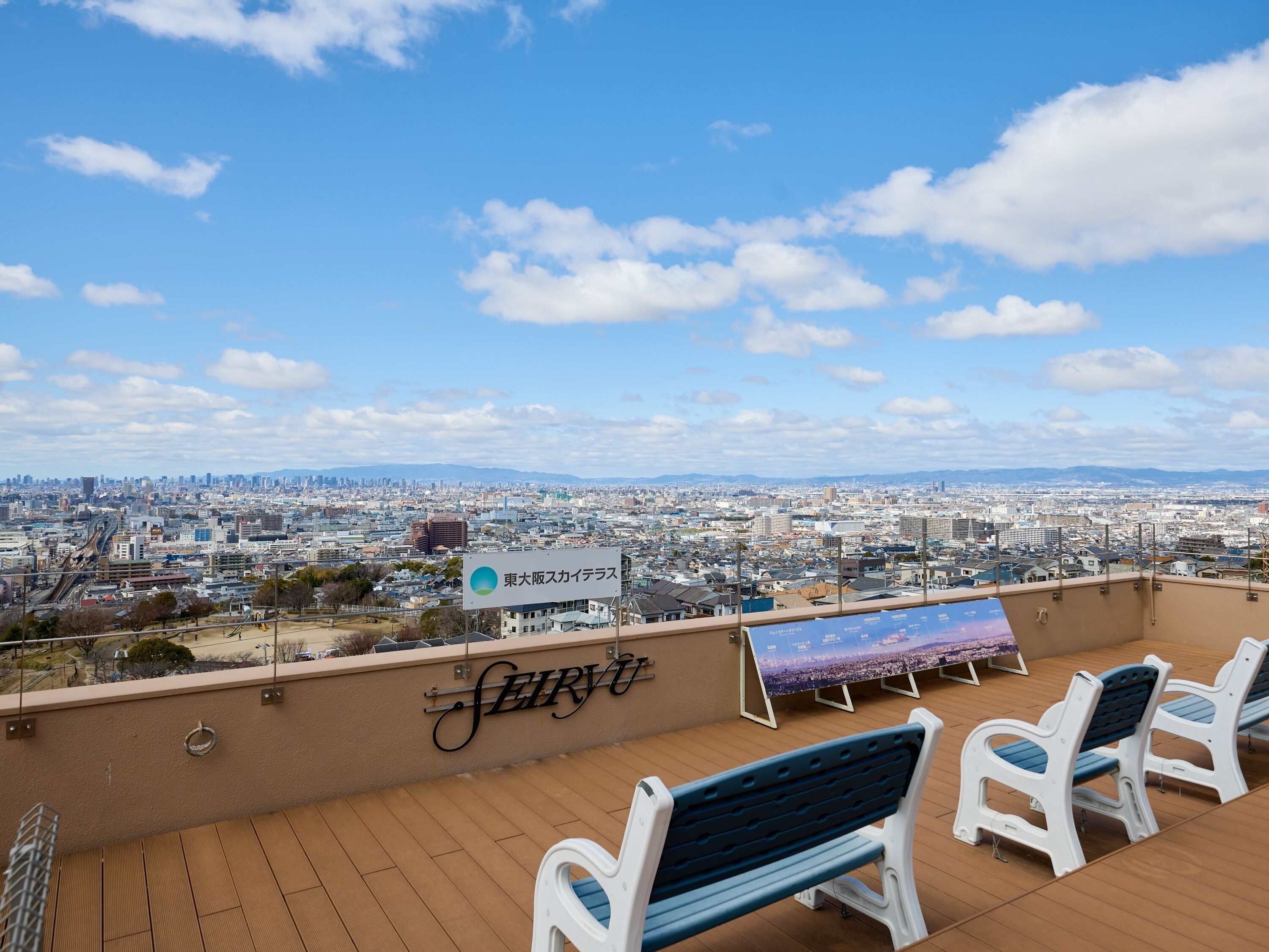 A rooftop terrace with a view of a cityscape, a sign for 'Seiryu,' and a few outdoor seating areas.