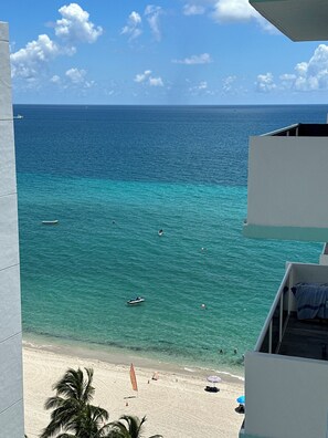 A beach view from a balcony with clear turquoise water, a sandy beach, and a few boats.