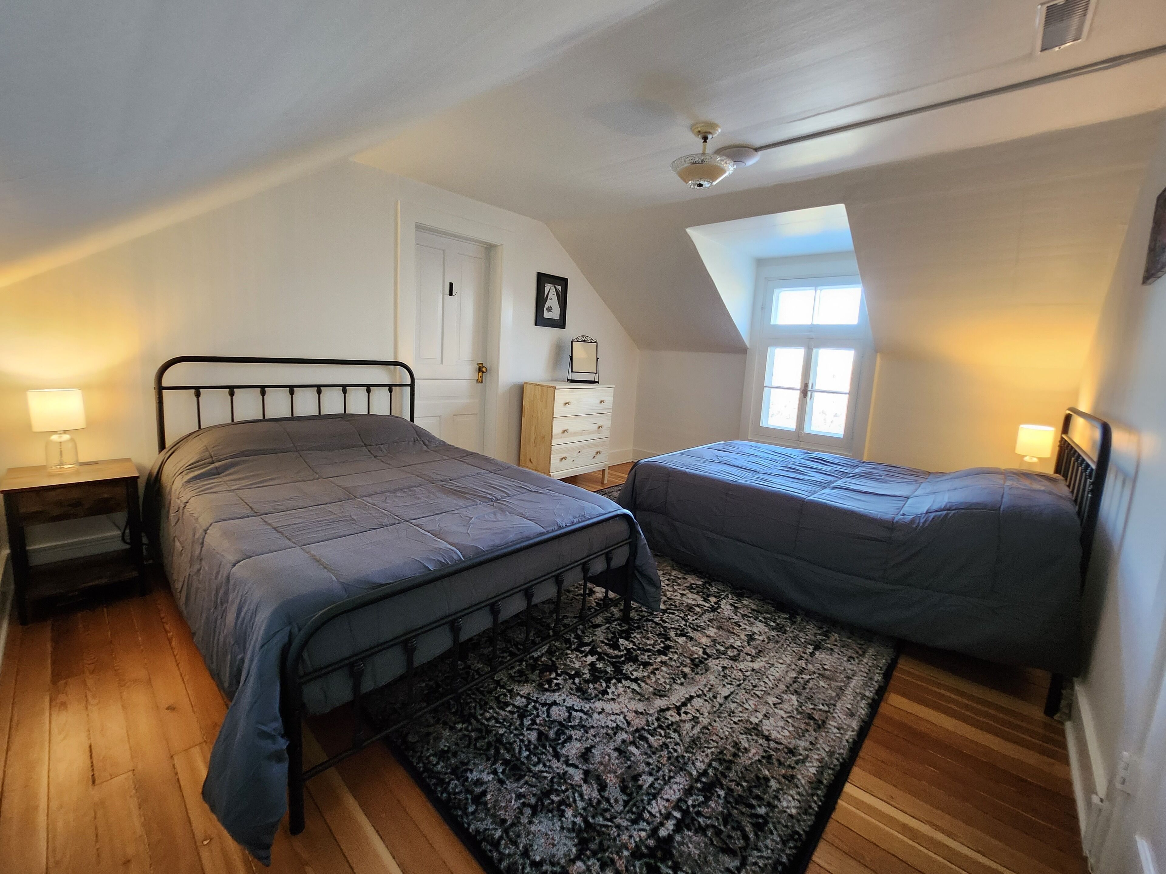 Une chambre avec deux lits, un plancher en bois, un ventilateur de plafond et une fenêtre.