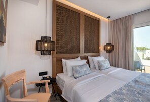 Habitación de hotel con cama, dos lámparas de noche, una silla, escritorio con teléfono y vistas al exterior.