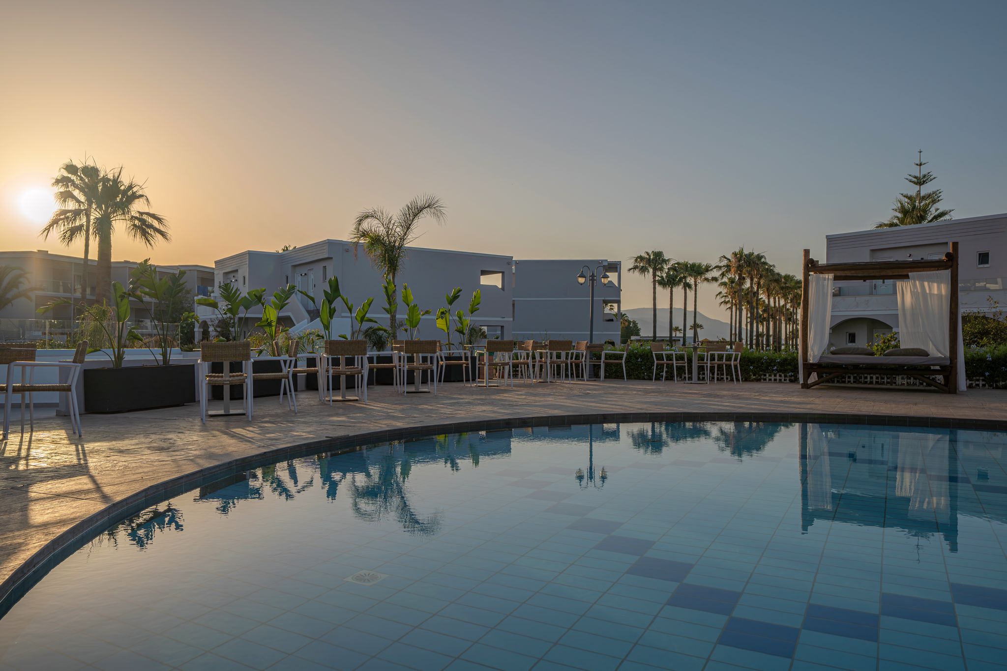A swimming pool with lounge chairs and a pergola, surrounded by palm trees and modern buildings.