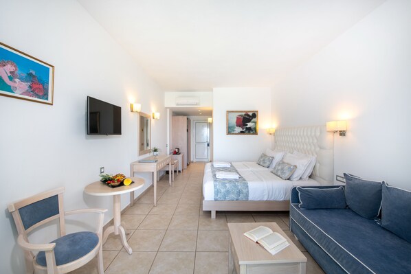 A hotel room with a bed, a sofa, a desk, a chair, a TV, and artwork on the walls. - Delfina Tropic Beach (Apokoronas)