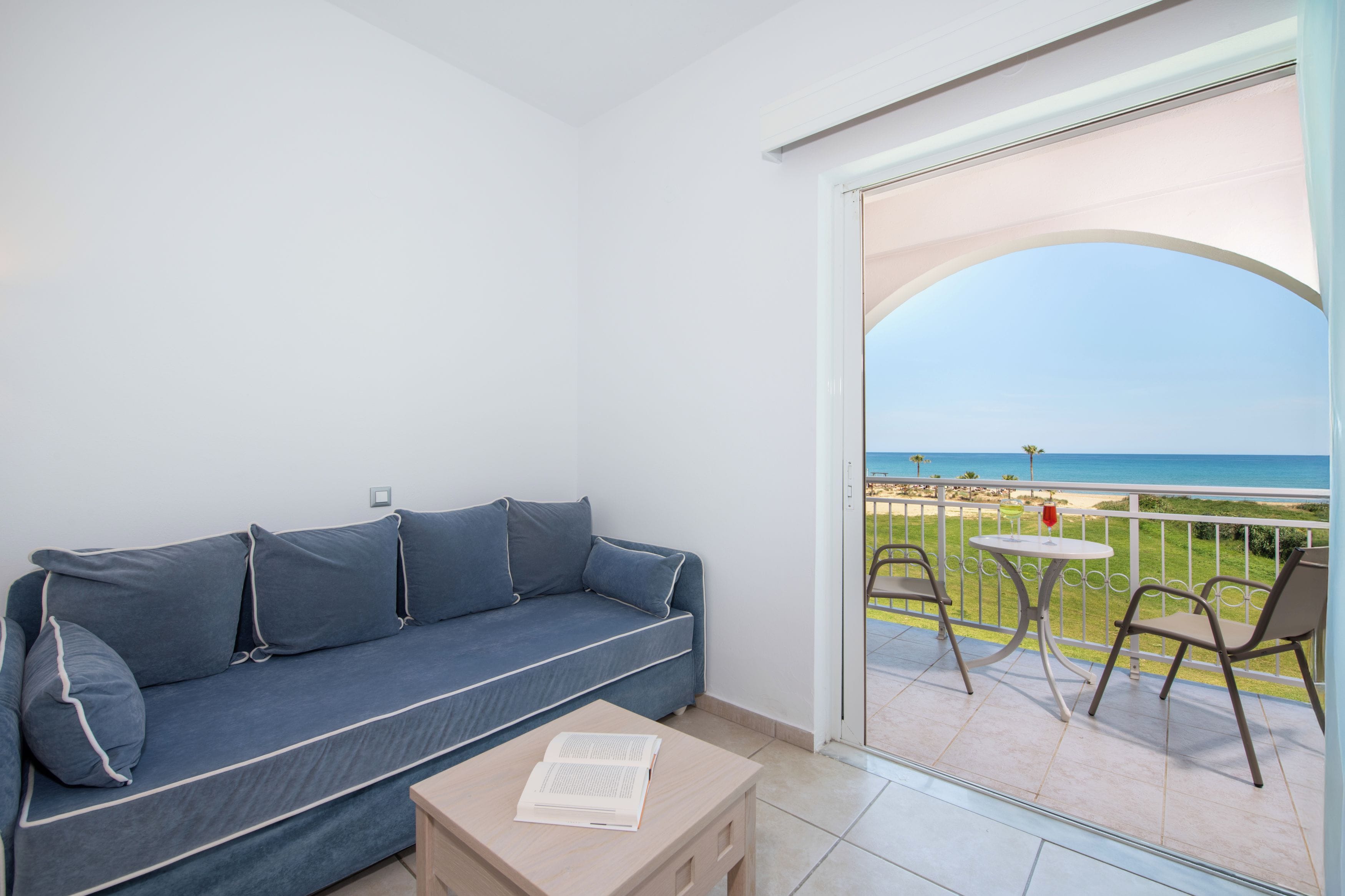 A balcony with a sofa, a table, and chairs, overlooking a beach.