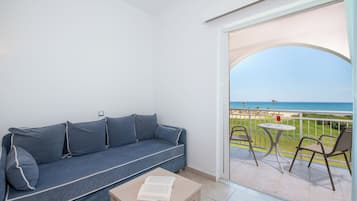 Varanda com sofá, mesa e cadeiras, com vista para uma praia.