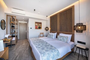 Una habitación de hotel moderna con una cama grande, cabecera de madera, zona de comedor con mesa y sillas, y un armario con espejo.