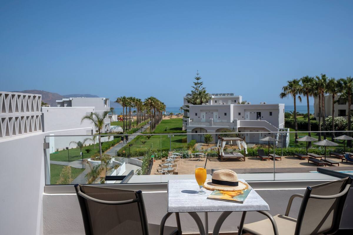 A balcony with a table, chairs, a drink, and a hat.