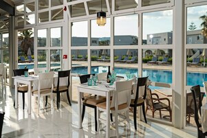 A poolside dining area with tables and chairs, a pool view, and a large window.