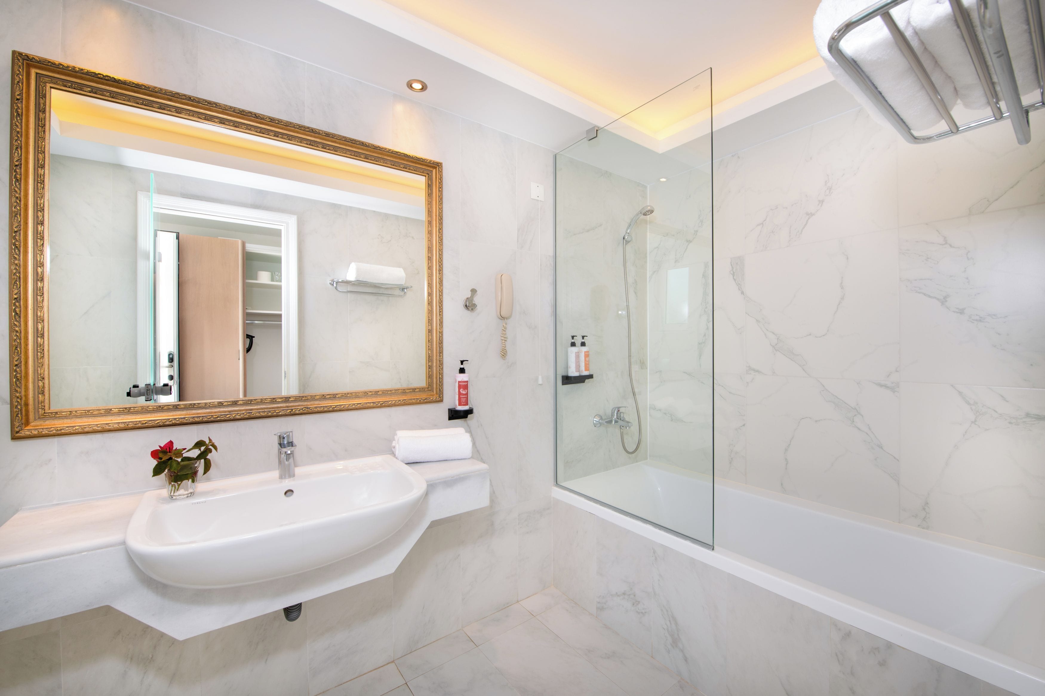 Un baño con un espejo grande, lavamanos, ducha con mampara de vidrio y retrete.