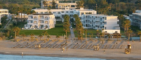 A coastal hotel with multiple buildings, a beach with sun loungers, and a view of the sea.