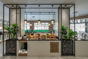A buffet area with a glass enclosure, hanging pendant lights, and potted plants. - Delfina Tropic Beach (Apokoronas)