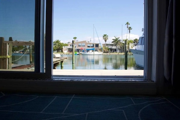 A view from a window of a marina with boats docked, palm trees, and buildings in the background.