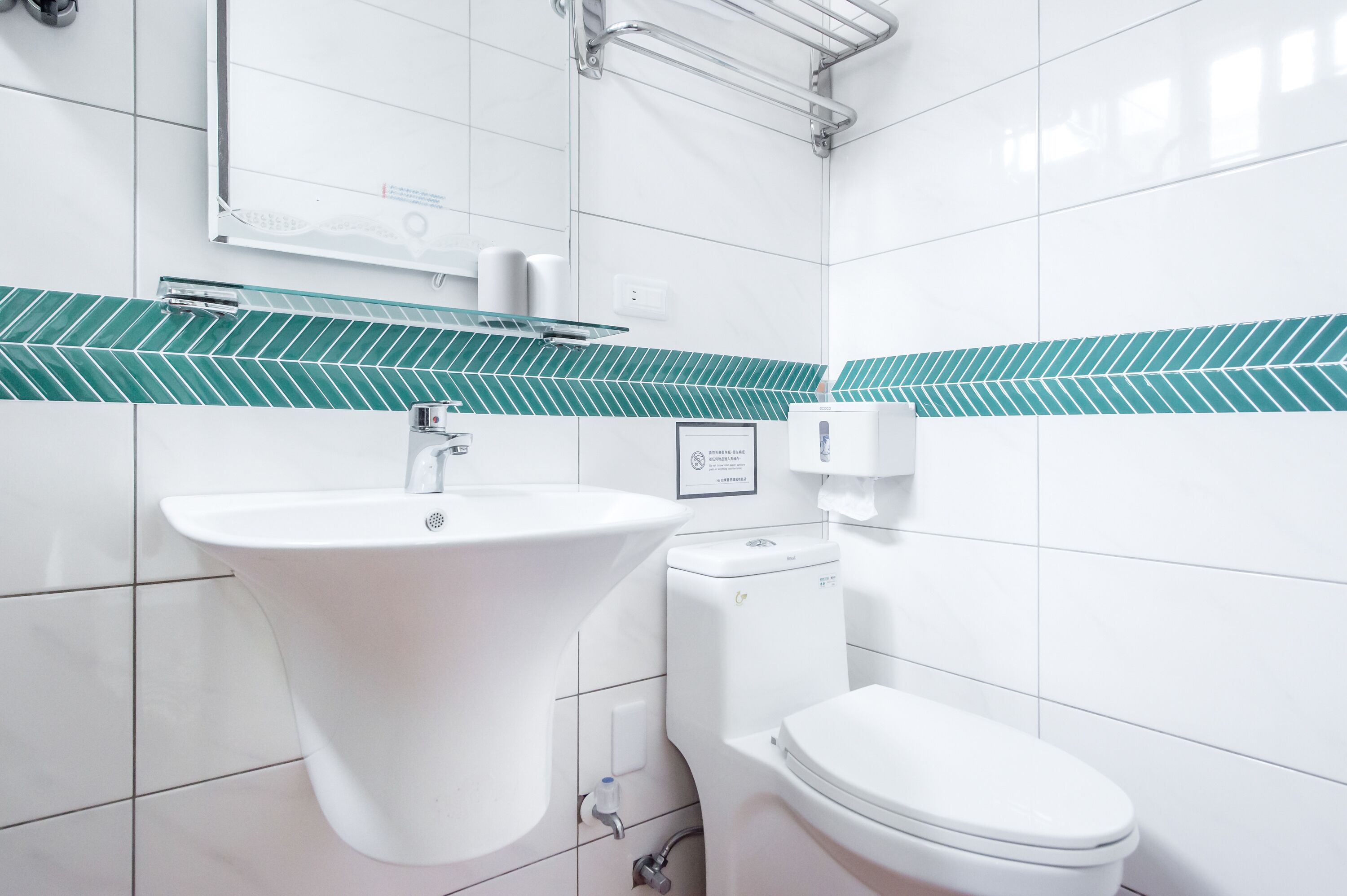 Un baño moderno con lavamanos, inodoro y salpicadero de azulejos verdes.