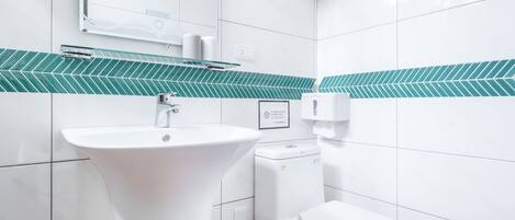 Un baño moderno con lavamanos, inodoro y salpicadero de azulejos verdes.