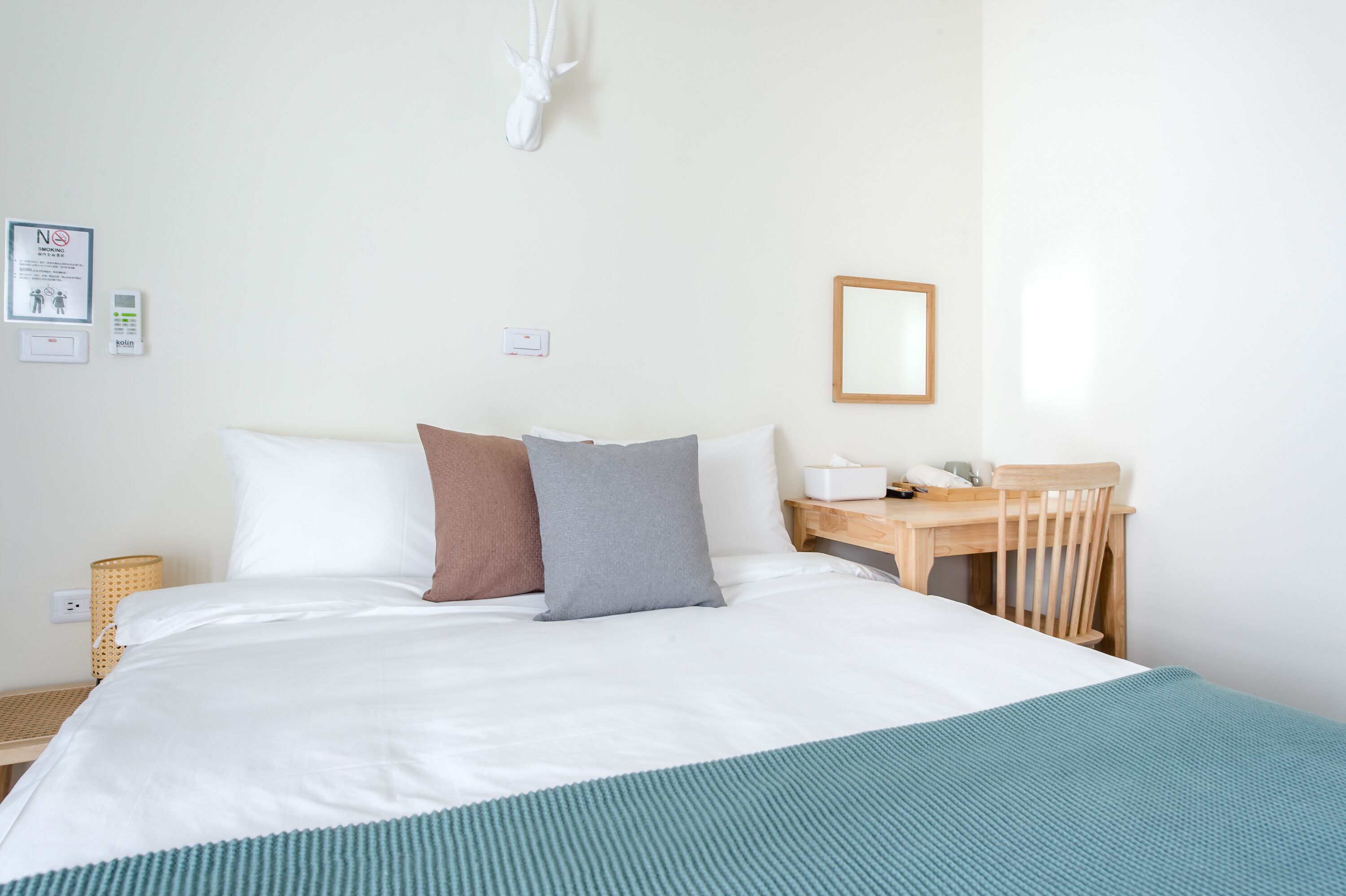 A hotel room with a bed, a wooden desk, and a chair. There is a wall-mounted light fixture and a framed picture on the wall.