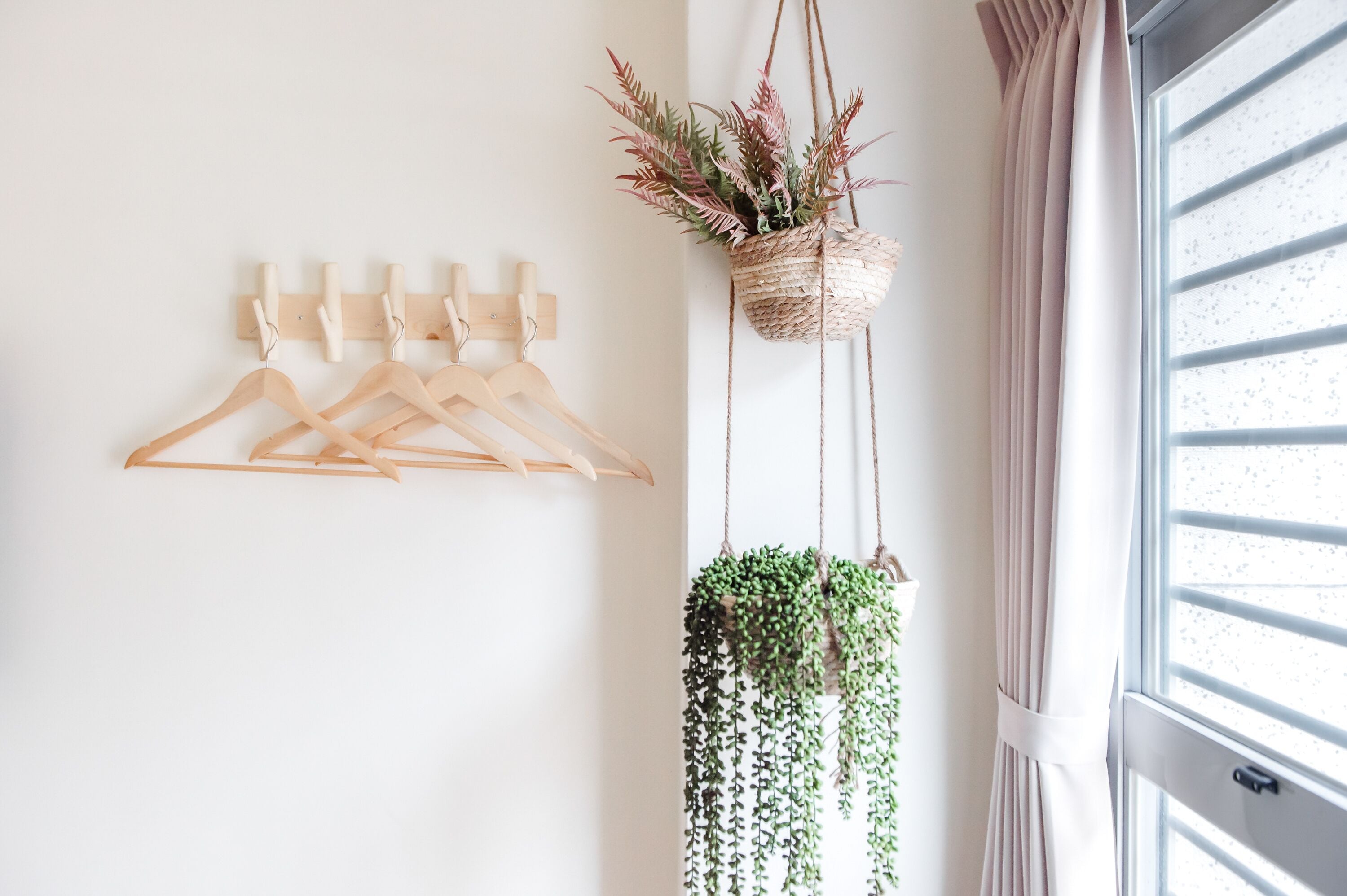 A room with wooden hangers on a wall, a woven plant hanger, and a window with curtains.