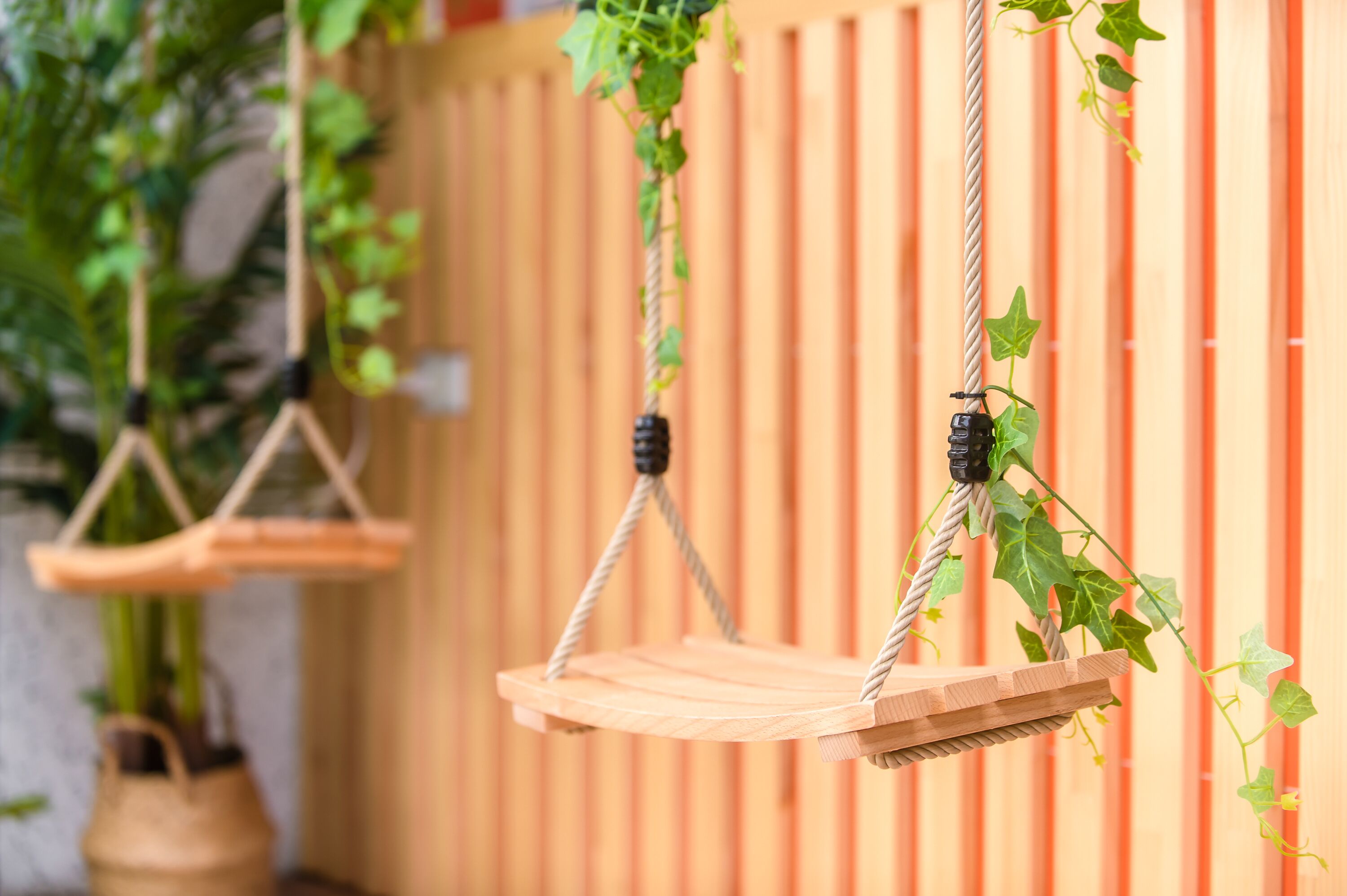 Una hamaca de madera suspendida con cuerdas, con una valla de madera al fondo.