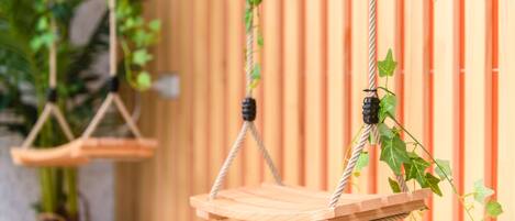 Una hamaca de madera suspendida con cuerdas, con una valla de madera al fondo.