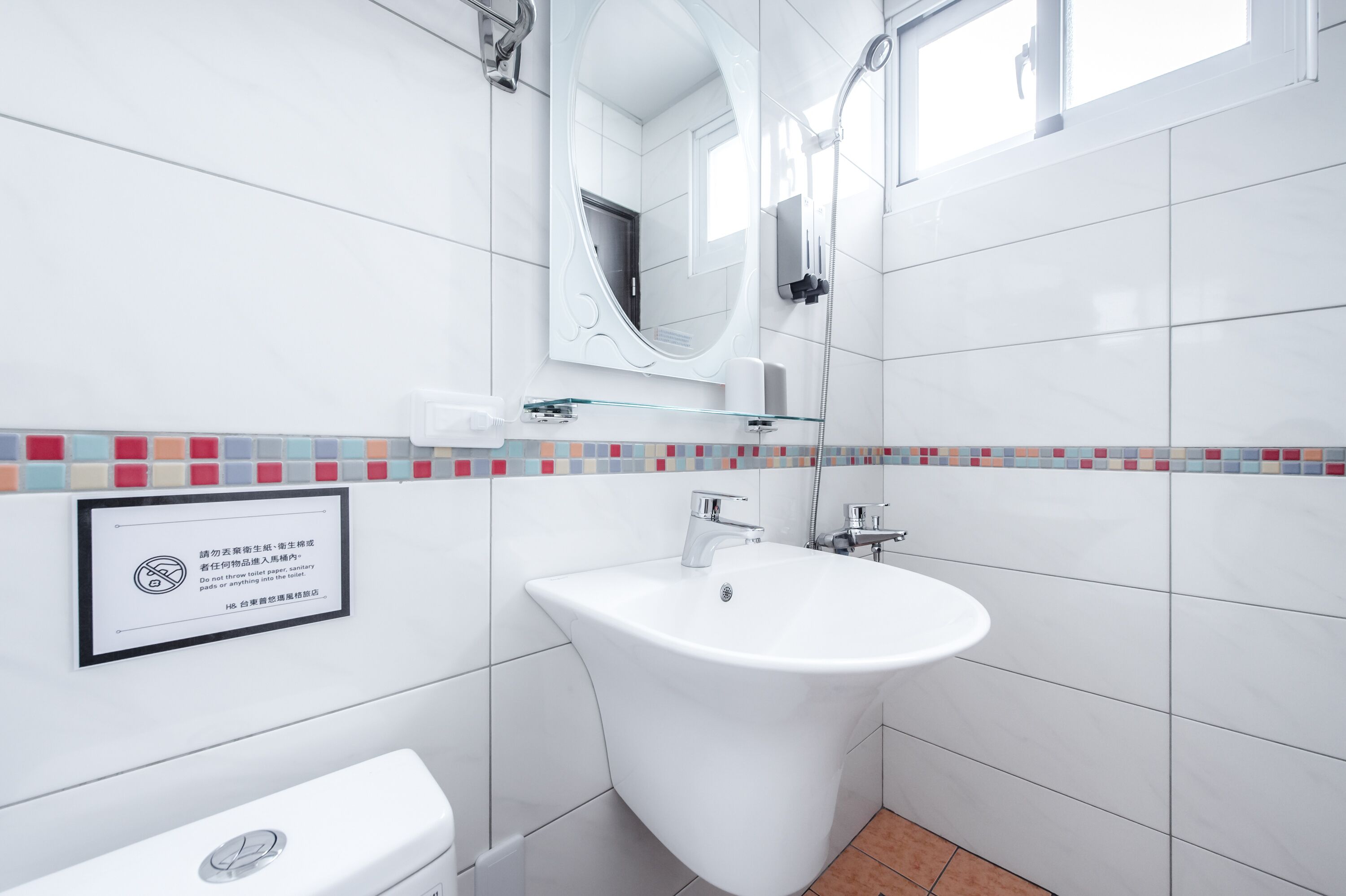 A modern bathroom with a white sink, a mirror, and a toilet. There is a sign on the wall with text.