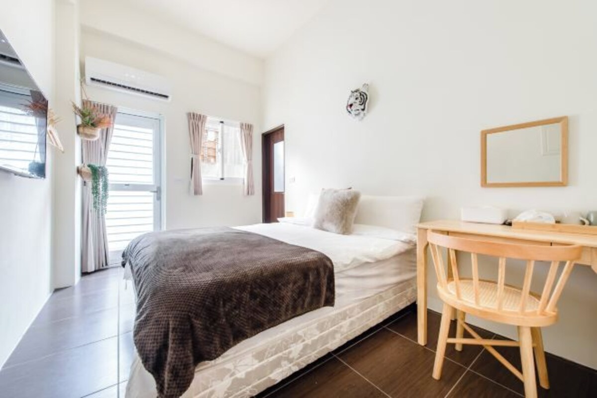 A bedroom with a bed, a wooden chair, a desk, and a mirror.