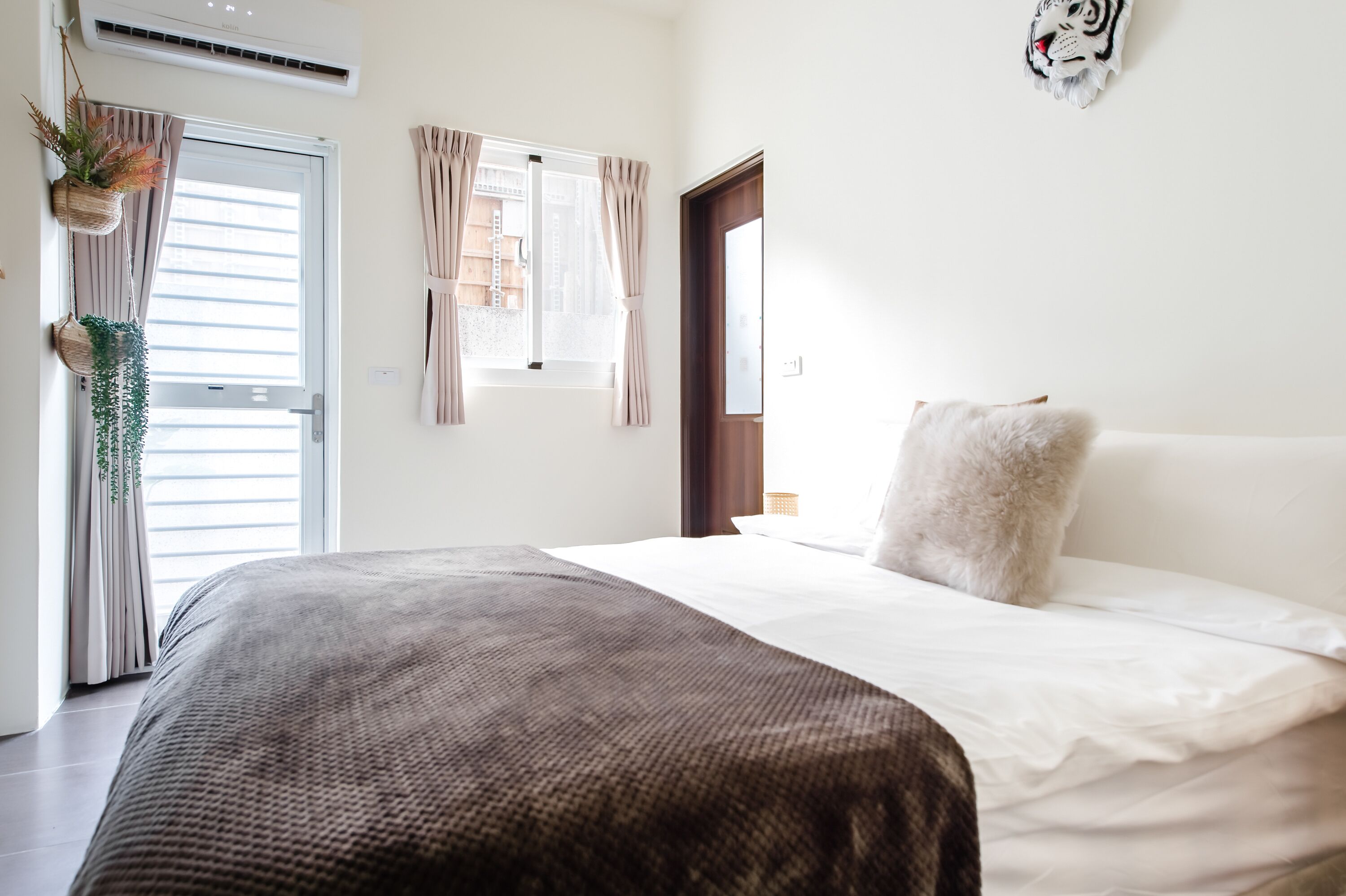 A bedroom with a bed, a window with curtains, a door, and a wall-mounted air conditioner.