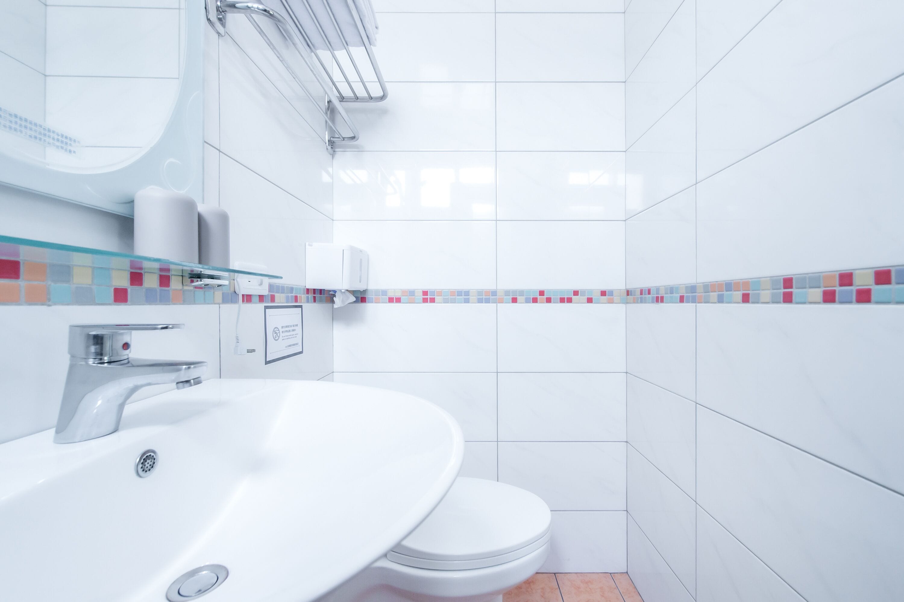 A modern bathroom with a white sink, toilet, and a glass shelf with toiletries.